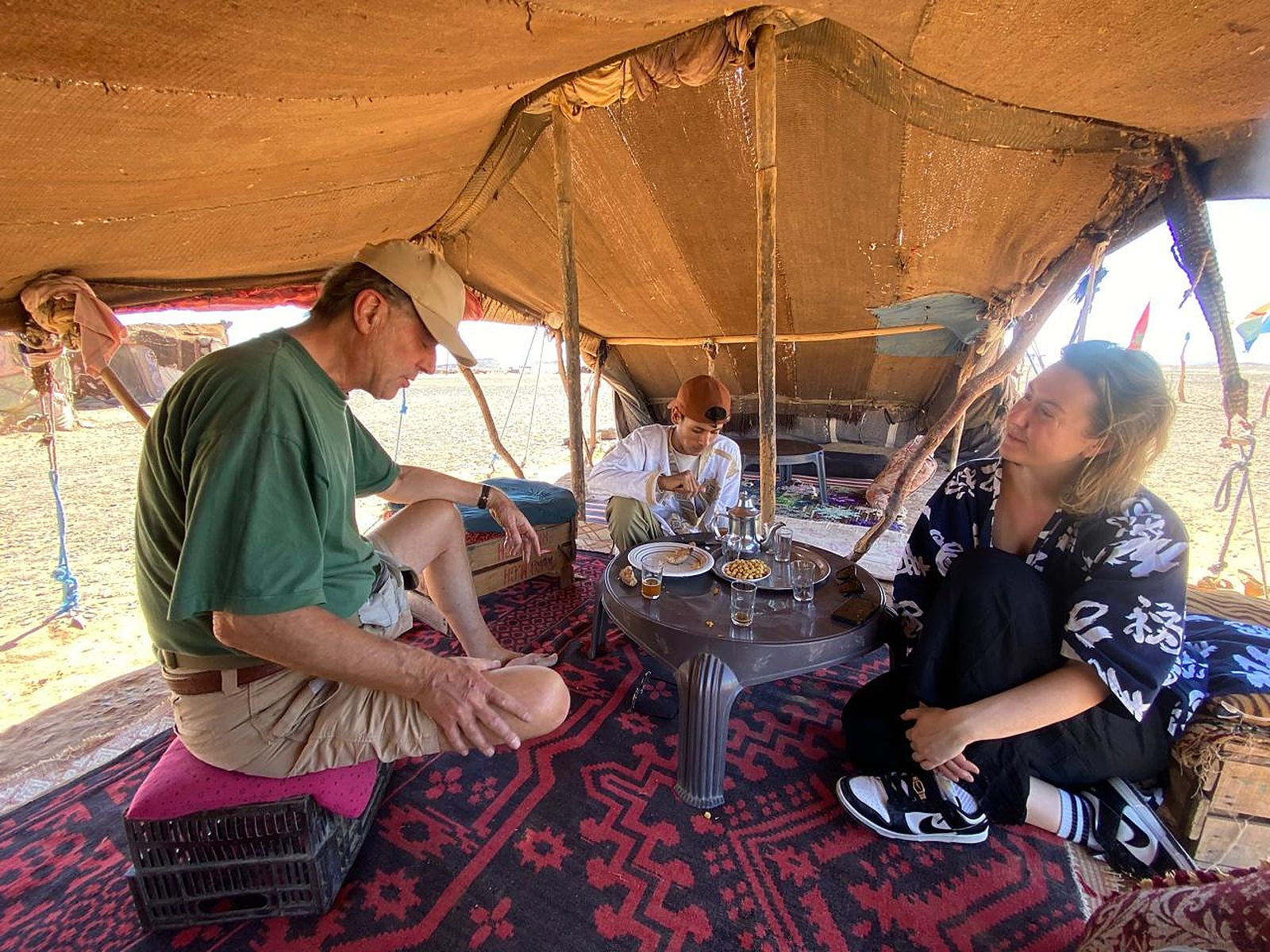 Travelers sharing traditional Moroccan mint tea with a Berber host inside a desert camp tent