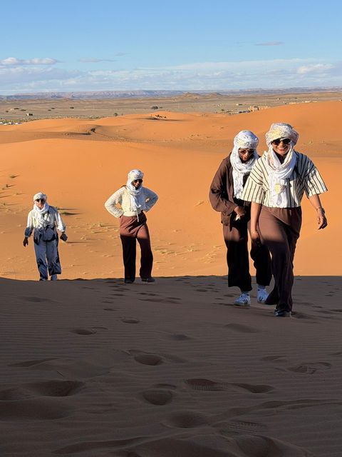 Travelers in desert headscarves walking along a high dune ridge near Merzouga