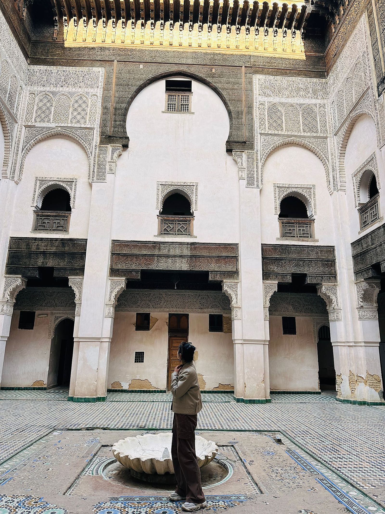 Traveler admiring the ornate courtyard of a historic medersa in the Fes medina, Morocco