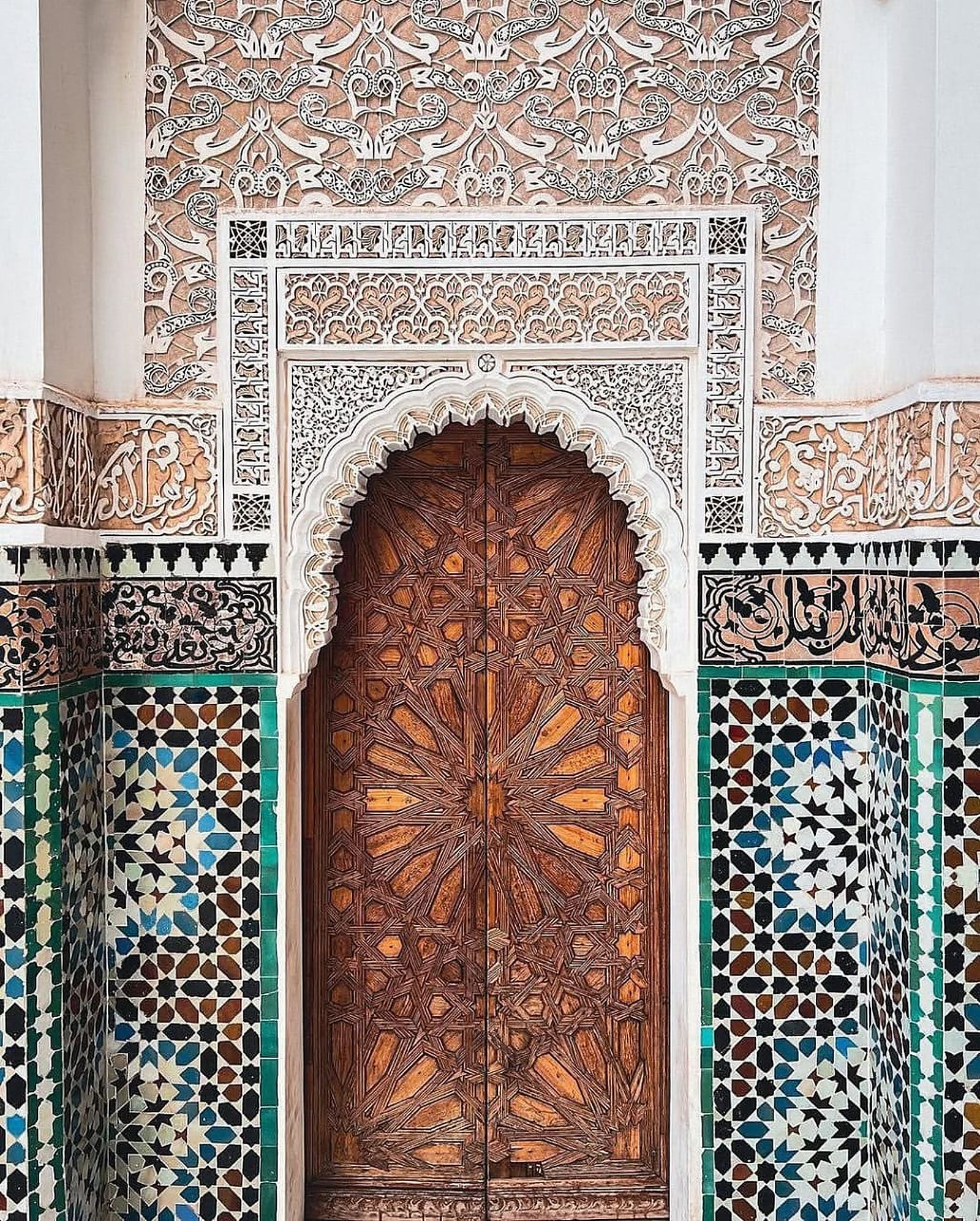 Ornate carved wooden door surrounded by traditional zellige tilework in Fes, Morocco