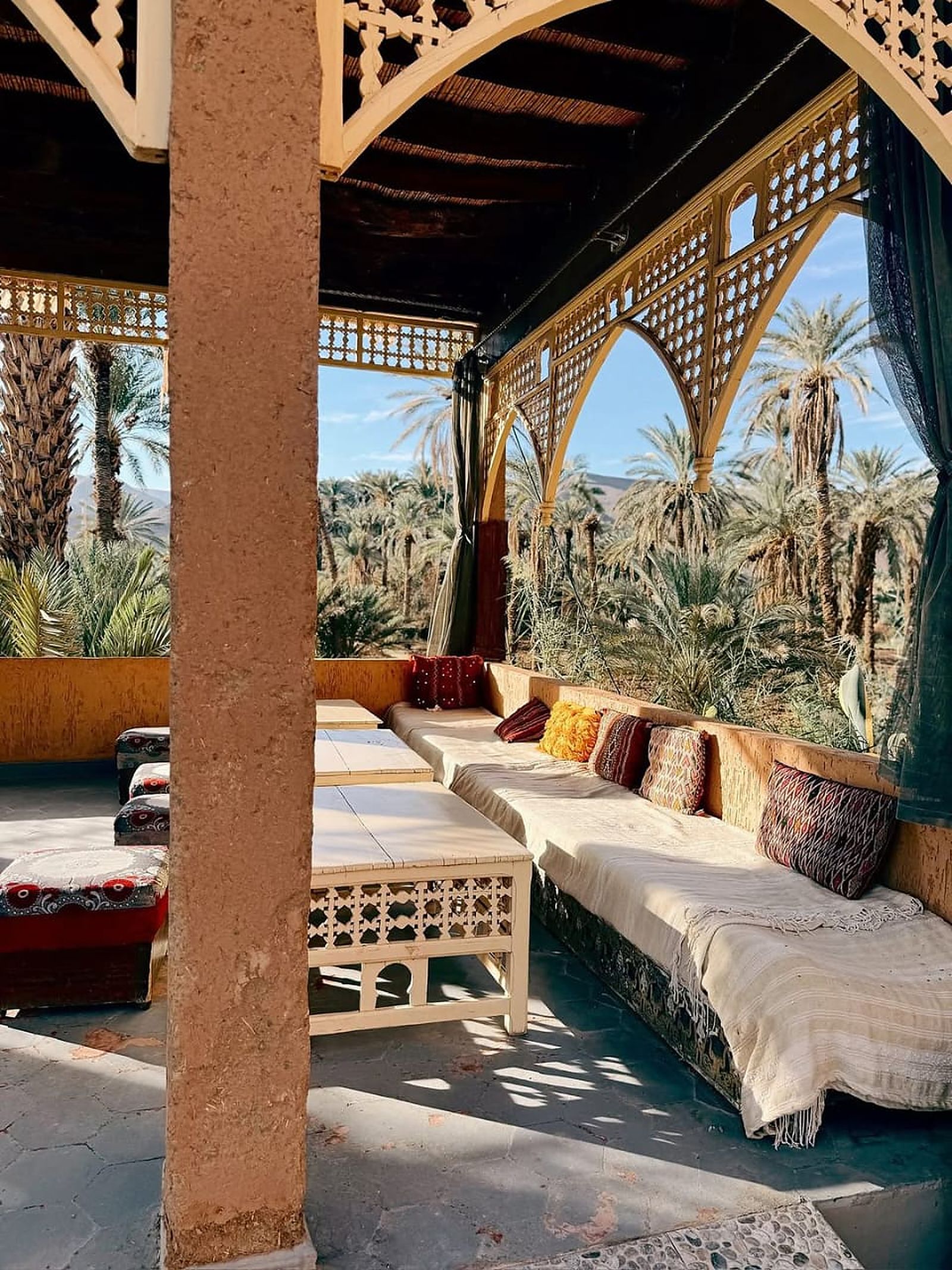 Shaded kasbah terrace lounge with cushioned seating overlooking a palm oasis in southern Morocco
