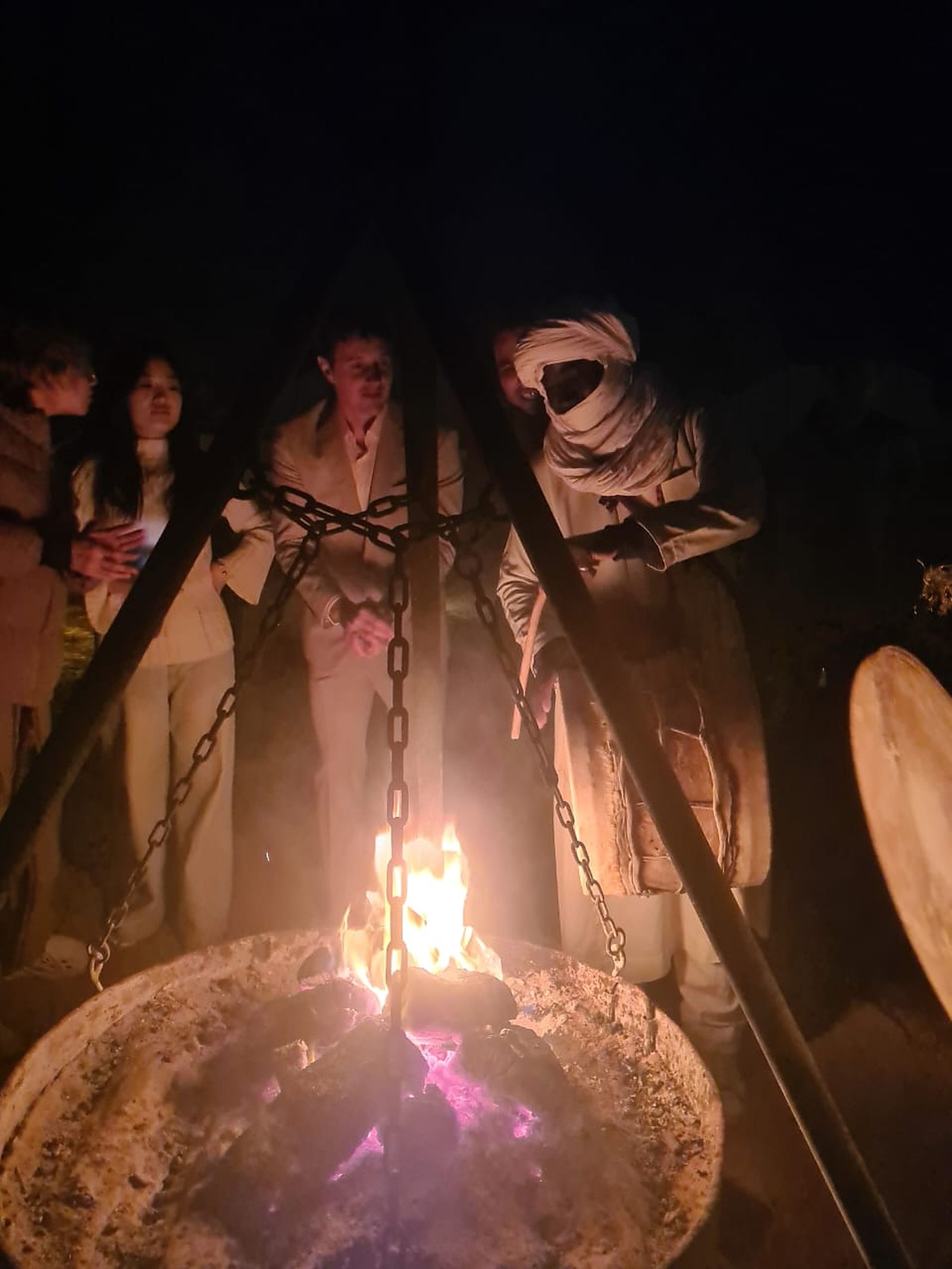 Travelers and a Berber guide gathered around the fire at a Sahara desert camp near Merzouga at night