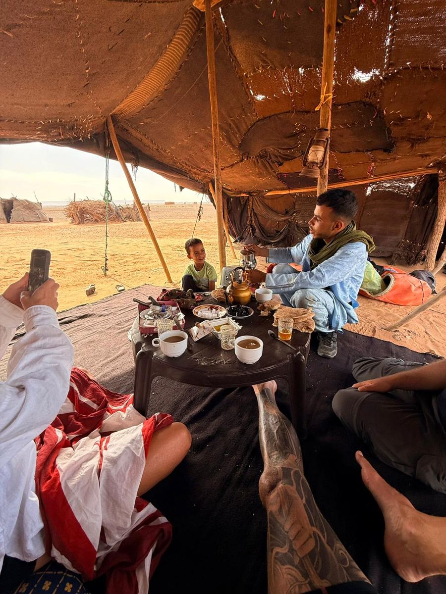 Traditional Moroccan mint tea being poured inside a Berber desert tent with fresh bread and dates on the table
