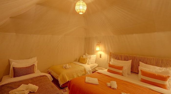 Deluxe en-suite desert camp tent with a hanging lantern and layered orange bedding
